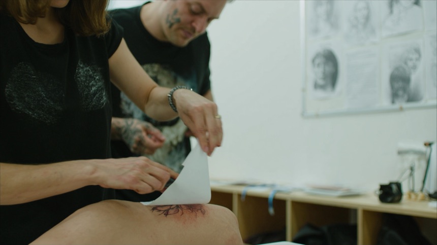 Alumna retirando el papel al aplicar un stencil de tatuaje sobre piel sintetica