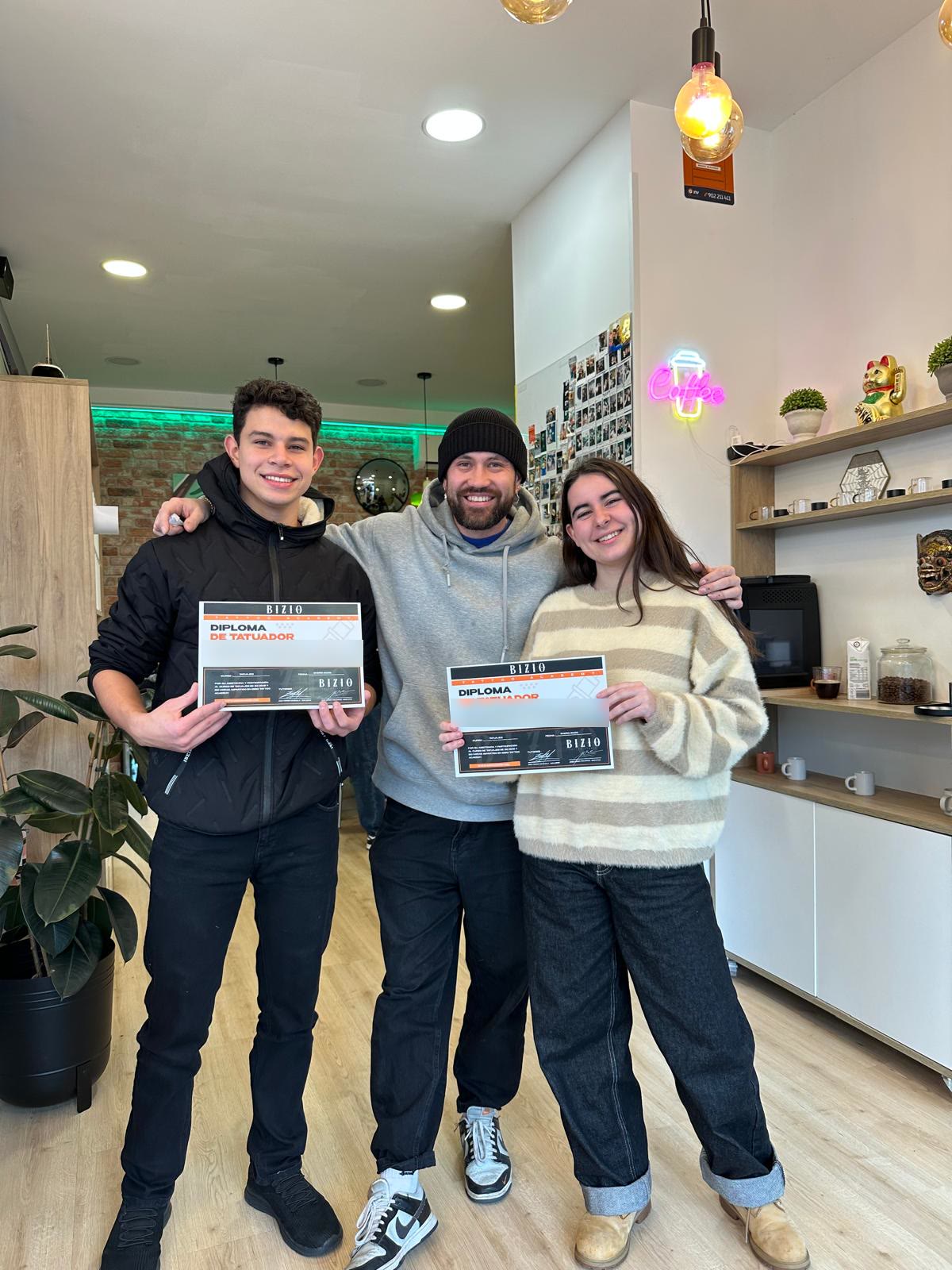 Dos alumnos con su diploma de tatuador junto a su profesor